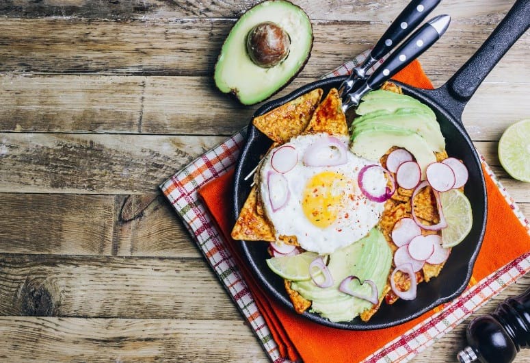 Chilaquiles with an egg on top next to an avacado